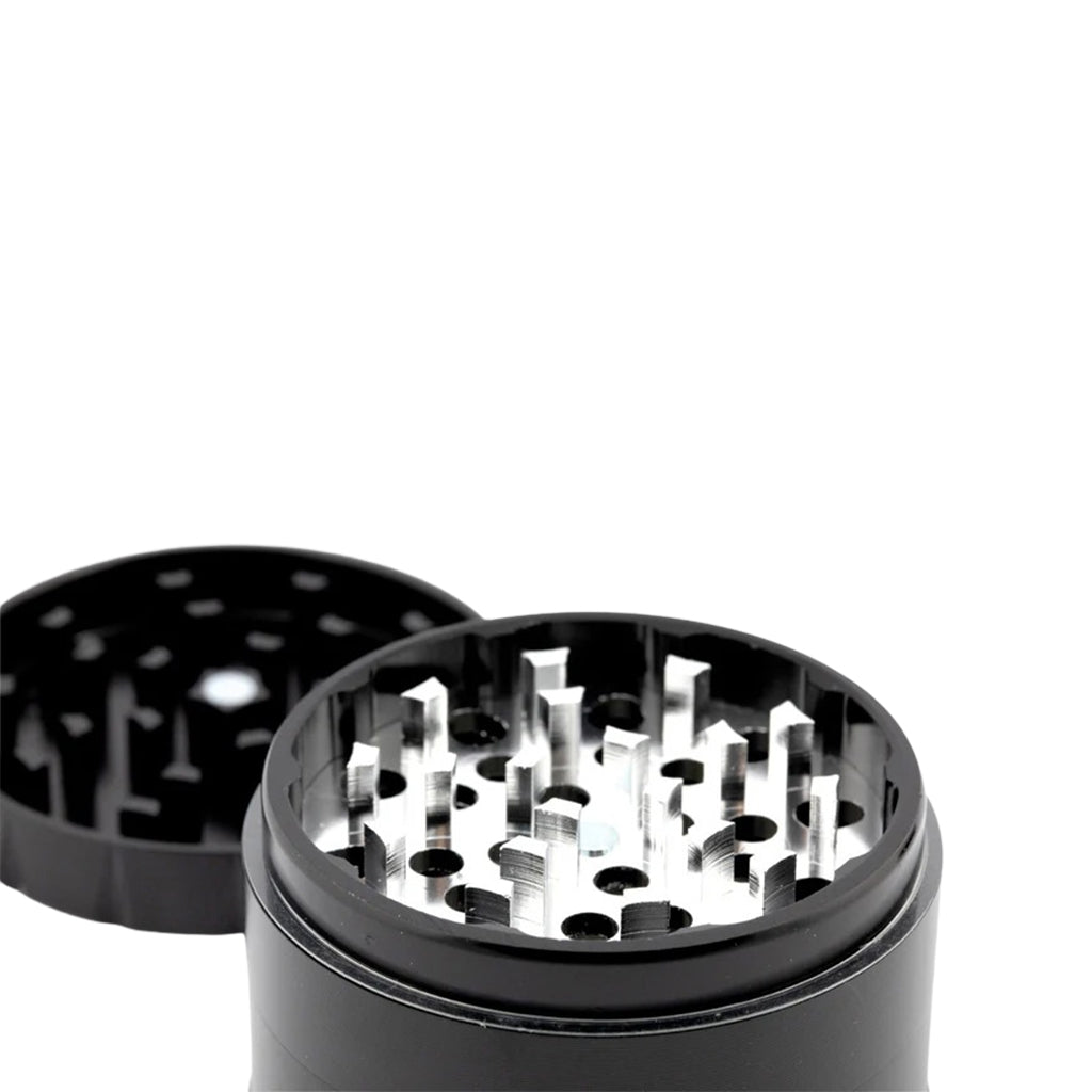 Close-up view of the GrindeROO OG herb grinder showing sharp aluminium grinding teeth and inner holes for herb flow, with the lid placed in the background.